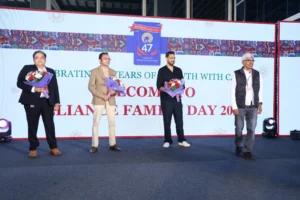 Four men standing on stage holding bouquets at a corporate family day event with branded backdrop and logo